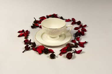 Beyaz bir sırtüstü uzanmış porselen bardak ve çiçek yaprakları.