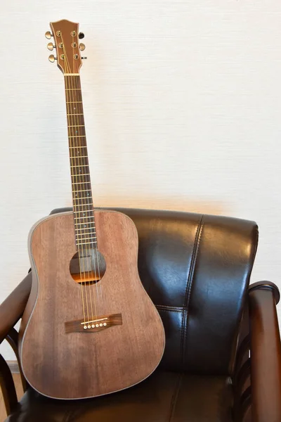 Acoustic six-string guitar and vintage leather armchair in the interior