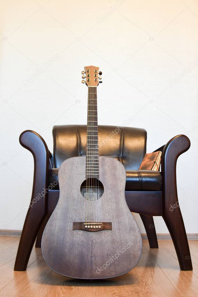 Acoustic six-string guitar, vintage leather armchair and vintage notepad in the interior