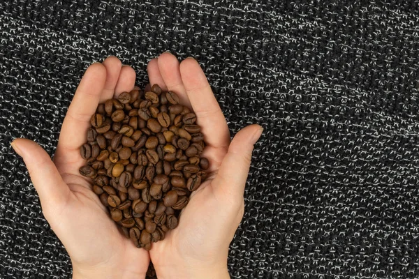Roasted coffee beans in the palms on a dark background top view with copy space