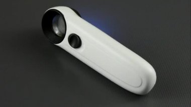 Aydınlatıcı. Bir kuyumcu büyüteci siyah arka planda döner. Üst görünüm.