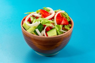 Domatesli sağlıklı salata, salatalık, zeytin, soğan, mavi arka planda seramik kasede salata. Sağlıklı yeme kavramı.