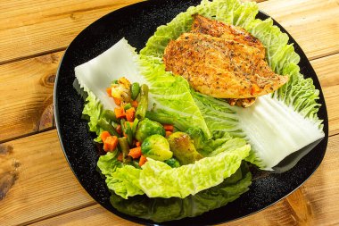 Izgara tavuk göğsü ve siyah tabakta marullu sebze karışımı. Yakın plan. Ahşap arkaplan