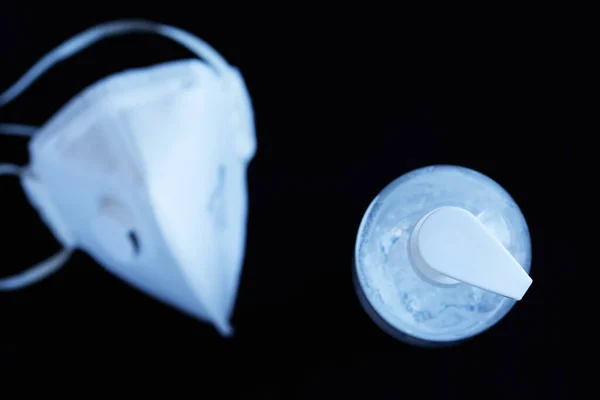 Siyah arka planda beyaz yüz maskesi olan şeffaf el dezenfektanı jeli beyaz berrak plastik bir şişe. Coronavirus covid-19, solunum hastalıkları ve sıhhi temizlik içeren viral salgınlar için kavram.