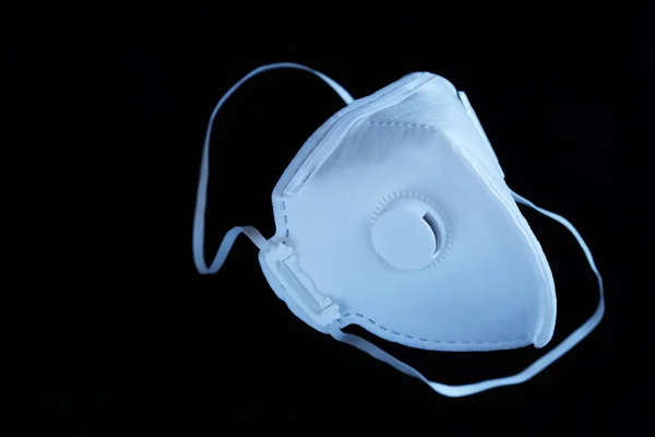 A non reusable sterile white ffp3 mask with valve on a black background. Concept for coronavirus covid-19, respiratory diseases due to allergies and air pollution