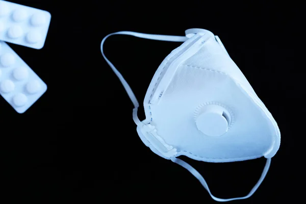 Siyah arka planda parasetamol gibi ağrı kesicileri olan steril olmayan beyaz bir ffp3 maske. Coronavirus covid-19 kavramı, alerji ve hava kirliliği nedeniyle solunum hastalıkları