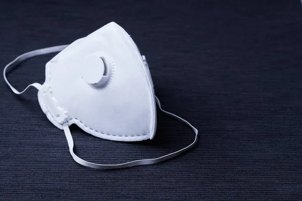 Koyu arkaplan üzerinde covid-19 corona virüsü, h1n1, h5n1 gibi virüslere karşı koruma olarak kullanılabilen, yeniden kullanılamaz, steril beyaz ffp3 kapakçıklı bir maske.