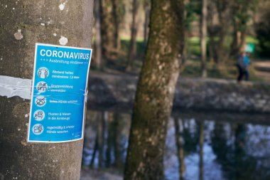 Munich, Germany - March 28, 2020: a note in German in the green areas of the city to inform the citizens of the safety measures to be taken due to covid-19 Coronavirus. The measures include social distancing and hygiene recommendations. clipart