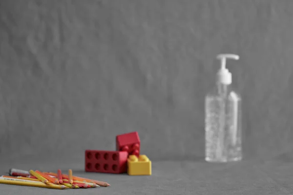 Üzerinde el dezenfektanı jeli, beyaz berrak plastik bir şişe ve gri arka planda renkli kalemler var. Coronavirus covid-19 konsepti, okulda evde eğitim ve hijyen, hapis ve karantina.