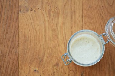 Sıcak meşe ağacından bir arka planda kaynayan mayalı hamurdan oluşan cam bir kavanozun yukarıdan çekimi. Sağlıklı yaşayan organik gıda kavramı, ev yapımı, diy, mide sağlığı, covid-19 coronavirüs mayası kıtlığı