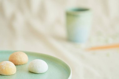 Yeşil bir tabakta üç parlak renkli mochis ve bej kumaşta bir kahve fincanı. Tatlı ve Asya yemeği, Japon kültürü ve gelenekleri, seyahat ve kutlamalar, çay ve kahve molası
