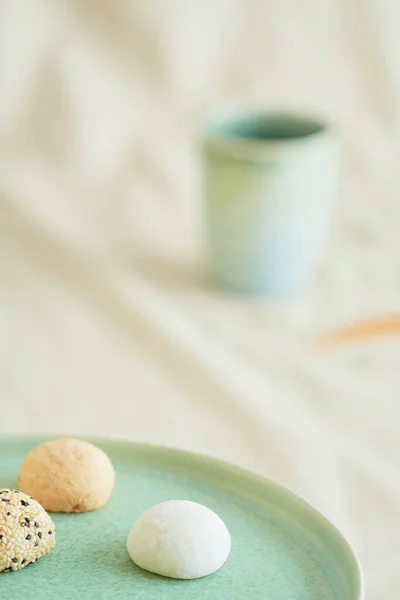 Yeşil bir tabakta üç parlak renkli mochis ve bej kumaşta bir kahve fincanı. Tatlı ve Asya yemeği, Japon kültürü ve gelenekleri, seyahat ve kutlamalar, çay ve kahve molası