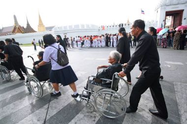 İnsanlar kıdemli tekerlekli sandalye üzerinde ibadet Kral cenazesi için yardım.