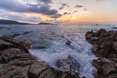 Taş sahil, köpüklü dalgalar ve güzel gün batımı. Tayland