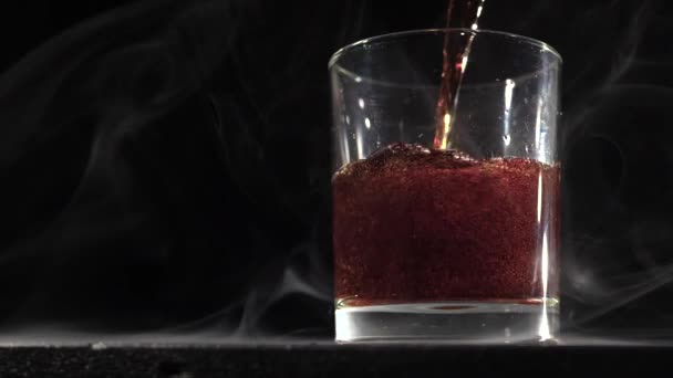 Into the glass pours cola on a black smoky background — Stock Video