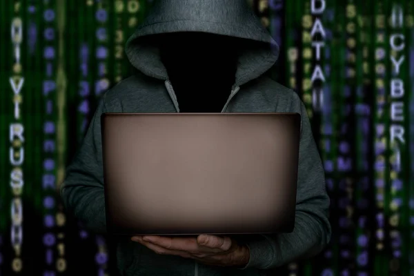 Хакер в капюшоне с ноутбуком в руке, стоит на фоне двоичного кода, киберпреступник запускает вирус . — стоковое фото
