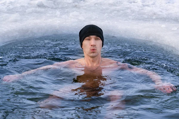 A man in a hat plunges into ice water in winter and takes his breath away — Stock Photo, Image