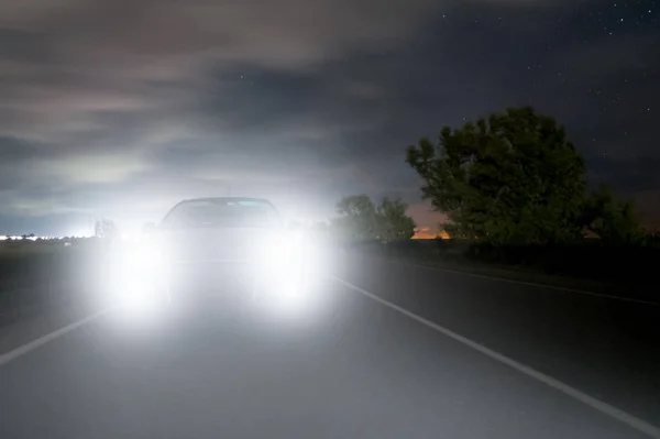 Um carro dirigindo ao longo de uma estrada noturna está se aproximando do escuro e é cego pelos faróis . — Fotografia de Stock