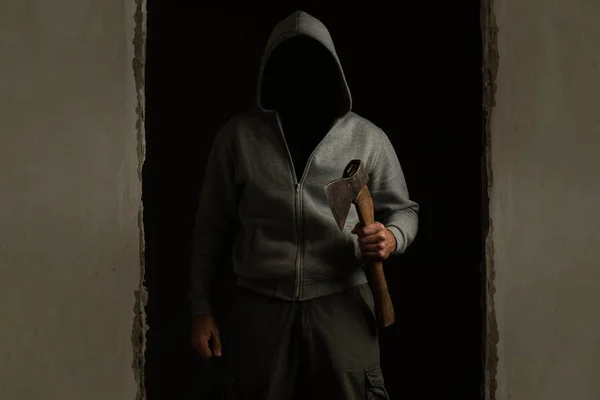 Unknown man with a hood on his head with an ax in his hand out of the dark room