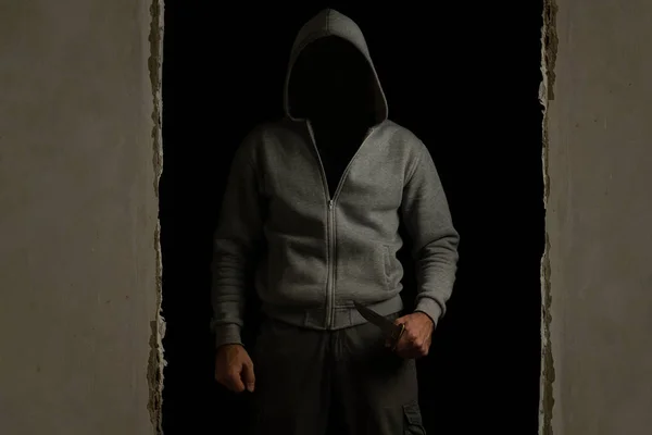 Unknown man with a hood on his head and a knife in his hand out of the dark room
