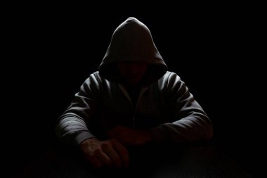 Kapüşonlu bir adam karanlıkta oturur ve kollarını ileri uzatır. Suç ve İnternet Güvenliği