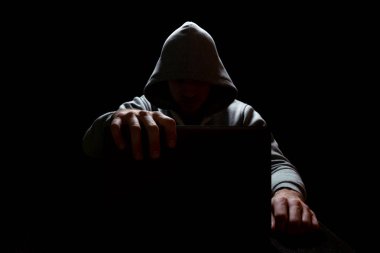 Kapüşonlu bir adam karanlıkta bir laptop kapağını kapatıyor, siber güvenlik, hackleme...