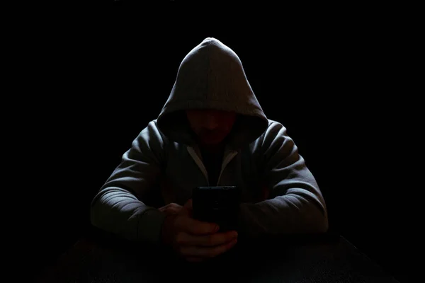 Telefon dolandırıcısı elinde bir telefonla karanlıkta, masada oturuyor.