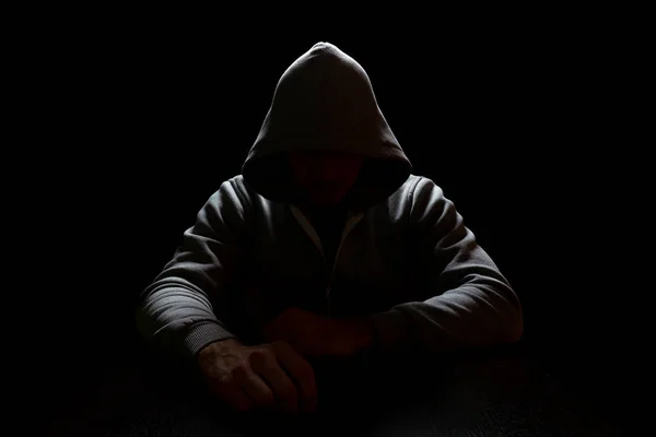 Человек в капюшоне сидит в темноте с вытянутыми вперед руками. Преступность и интернет-безопасность — стоковое фото