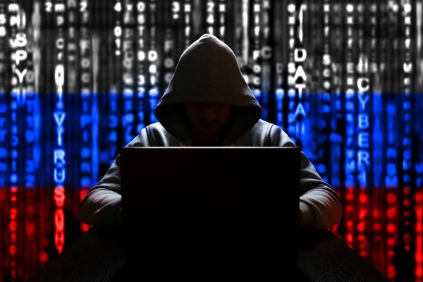 Rusya 'dan bir hacker, ikili koddan Rusça' nın üç renkli arka planına karşı bilgisayar başında çalışıyor.