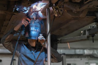 Kaynak metal ürünleri. Maskeli kaynakçı araba tamiri yapıyor.