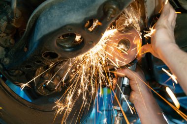 Paslı araba süspansiyonlarını öğütücüyle keserek, yakın plan. Öğütücüden kıvılcımlar