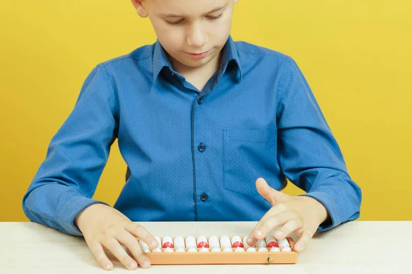 The boy sits at table and thinks on the soroban. Mental arithmetic