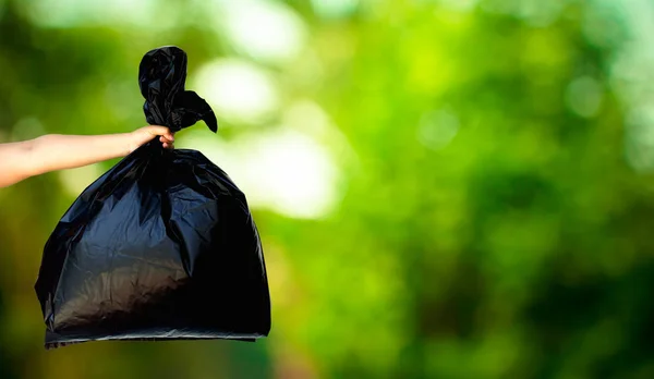 Lidská ruka ukazuje pytle na odpadky na svěží zelené přírody rozmazané pozadí — Stock fotografie