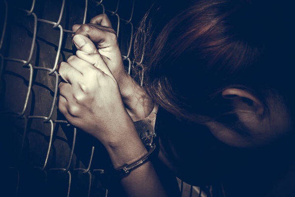 Sad woman with handcuffs holding rust metal fence