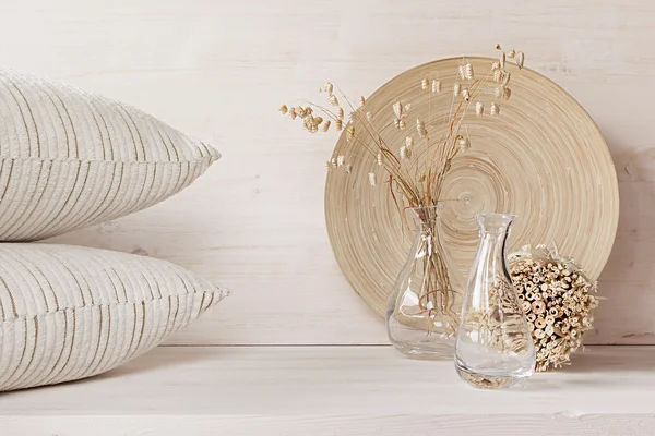 Soft home decor of  glass vase with spikelets and pillows on white wood background.