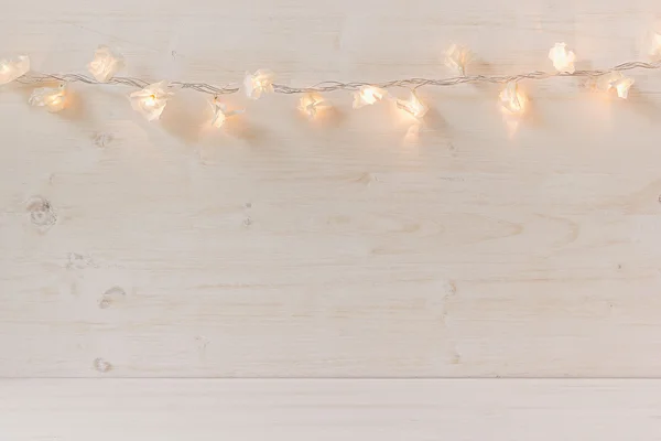 Christmas lights burning  on a white wooden background.