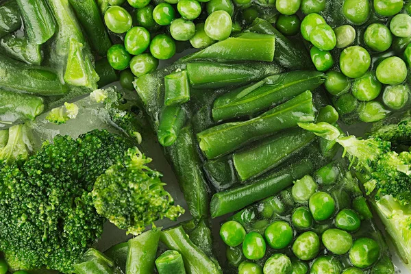 Sortiment čerstvých zmrazených zelený hrášek, fazol obecný, brokolice s detailním jinovatka jako pozadí. — Stock fotografie