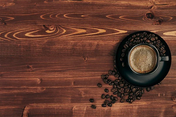 Heißer Kaffee in schwarzer Tasse mit Crema und Bohnen mit Kopierraum auf braunem alten Holzbretthintergrund, Draufsicht. — Stockfoto