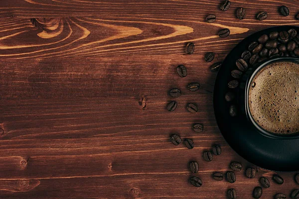Горячий кофе в черной чашке с кремом и бобами с копировальным местом на старом коричневом фоне деревянной доски, вид сверху . — стоковое фото