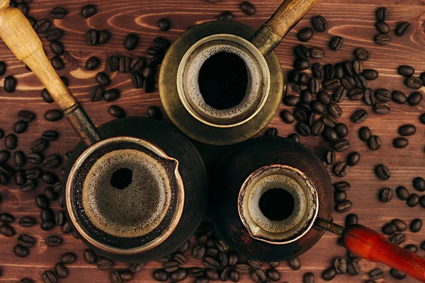 Gorąca kawa w shabby turecki garnki cezve z crema, fasola na brązowy stare podłoże drewniane deska, widok z góry. — Zdjęcie stockowe