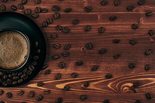 Gorąca kawa w czarny kubek z crem i wzór ziarna z kopia miejsce na brązowy stare podłoże drewniane deska, widok z góry. Styl rustykalny. — Zdjęcie stockowe