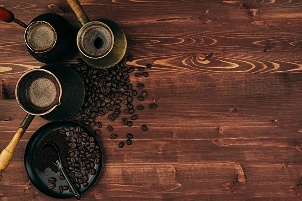 Горячий кофе в потрепанных турецких горшках cezve с бобами, блюдце с копировальным местом на коричневом старом деревянном фоне доски, вид сверху . — стоковое фото