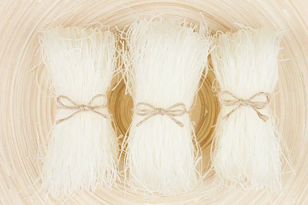 Sheaf raw asian noodles on soft beige wooden board with copy space, top view. — Stock Photo, Image