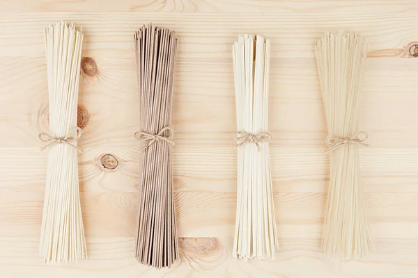 Assortimento fasci di tagliatelle asiatiche crude da vicino su sfondo bianco bordo di legno, vista dall'alto . — Foto Stock