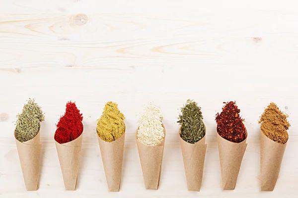 Colorful scattered powder seasoning in paper corners on white wooden board with copy space. — Stock Photo, Image