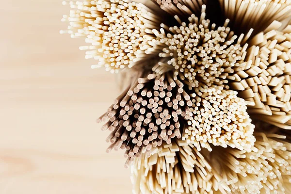 Cross-section of different bundles of raw noodles close up on soft beige wooden board, top view. — Stock Photo, Image