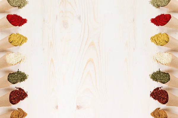 Декоративная граница различных специй порошка крупным планом в бумажных углах на белой деревянной доске с копировальным пространством . — стоковое фото