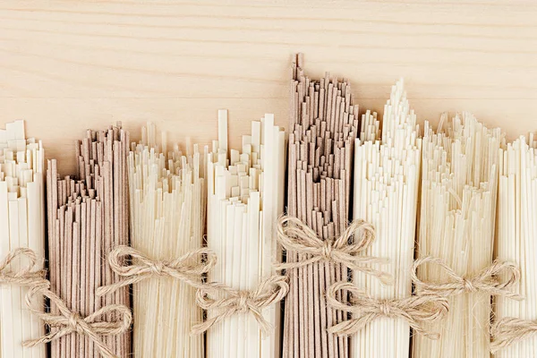 Diferentes paquetes de fideos asiáticos crudos de cerca sobre fondo de tablero de madera beige, vista superior . — Foto de Stock