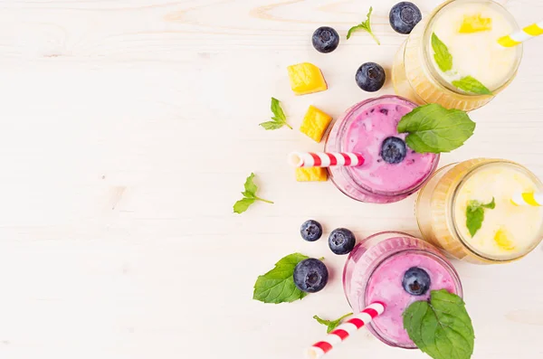 Čerstvé žluté a fialové ovocné smoothie ve skle sklenice s sláma, listy máty, mango plátky a berry, pohled shora. Měkké bílé dřevěné desce pozadí, kopírování prostor. — Stock fotografie