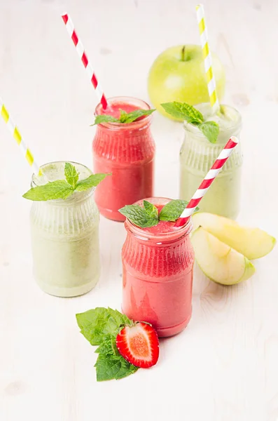 Batido de frutas verdes y rojas recién mezclado en frascos de vidrio con paja, hojas de menta de fresa y manzanas. Fondo de tablero de madera blanco, espacio de copia . —  Fotos de Stock